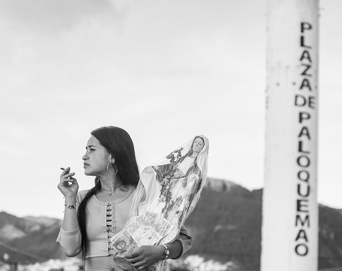 Fotograma del cortometraje Paloquemao. La protagonista fuma un cigarrillo en el exterior de la plaza de Paloquemao, sosteniendo una virgen de gran tamaño en cerámica. 